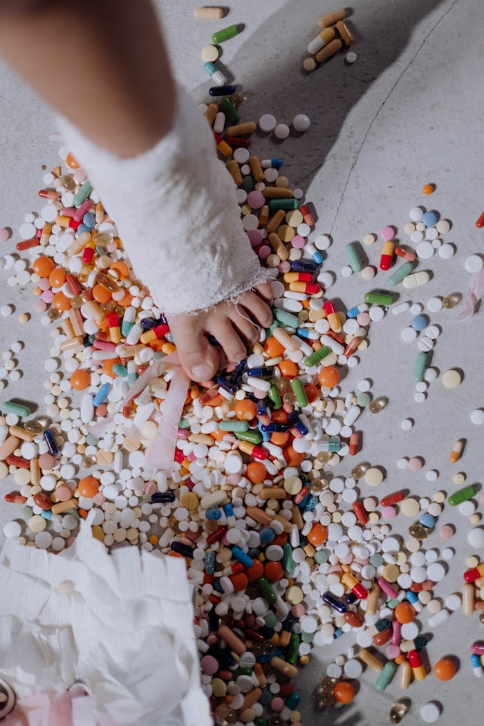 An overhead shot of a child's foot in a cast surrounded by scattered colorful pills indoors.
